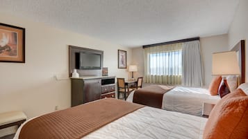 A hotel room with two beds, a desk, a television, and a window with curtains.