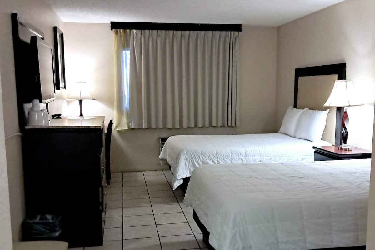 Una habitación de hotel con dos camas, un escritorio, una silla y un ventanal con cortinas.