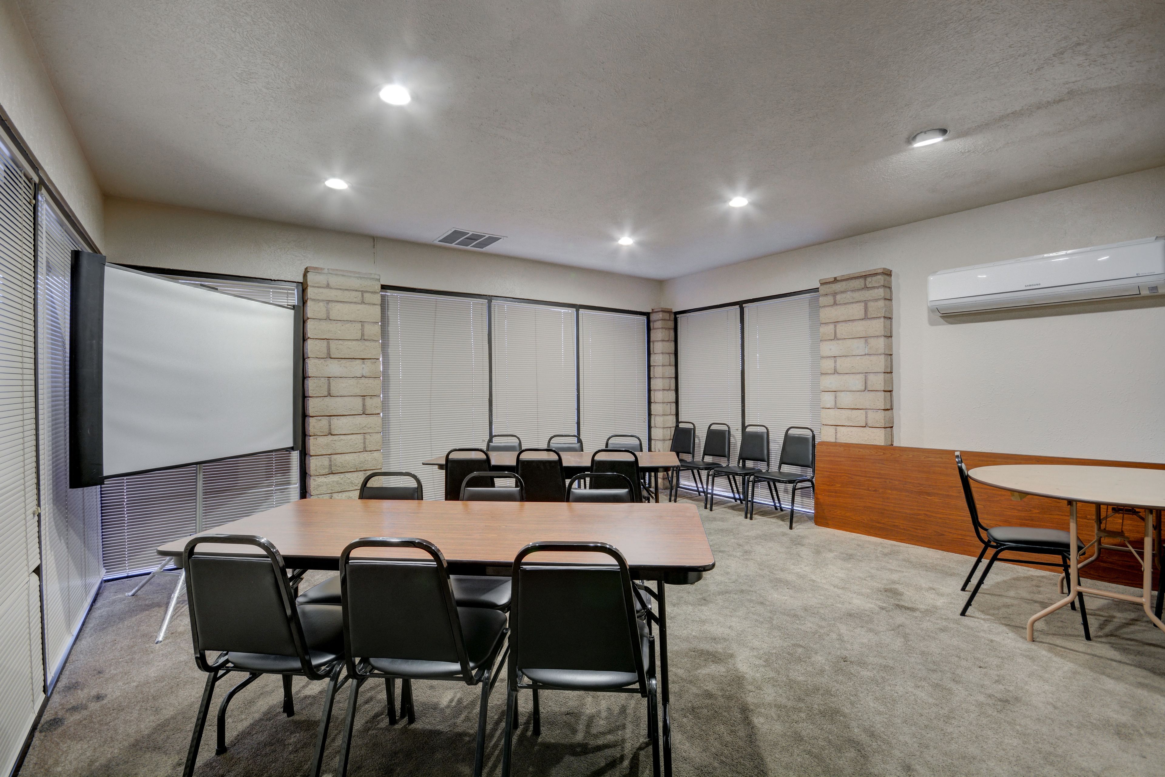 A conference room with a large table, chairs, a projector screen, and an air conditioning unit.