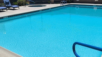 Una piscina azul cristalina con una escalera azul, sillas de descanso y una pared de ladrillo al fondo.