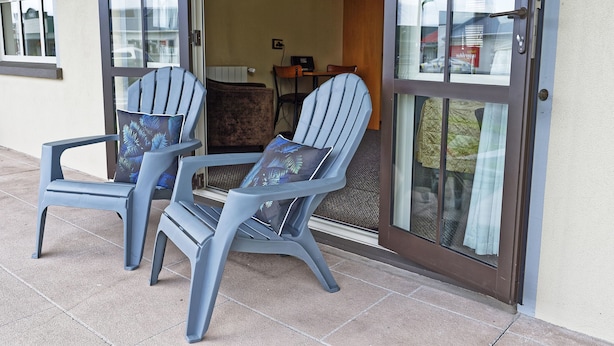 Two blue Adirondack chairs with patterned cushions outside a building with a sliding glass door. - Lantern Court Motel (Reefton)