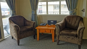 Two armchairs facing each other with a small wooden table between them, a laptop on the table, and a window with curtains. - Lantern Court Motel (Reefton)