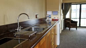 A kitchen with a stainless steel sink, wooden cabinets, and a view of the room through a window. - Lantern Court Motel (Reefton)