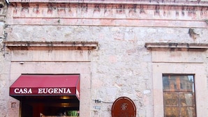 L’entrée d’un immeuble à la façade en pierre, surmontée d’une marquise rouge portant l’inscription « CASA EUGENIA ».