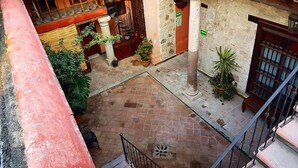 Une cour avec un sol carrelé, des plantes en pot, un escalier et une colonne.