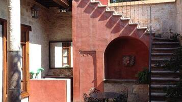 A courtyard with a stone staircase, a round table with metal chairs, and a rustic building facade.