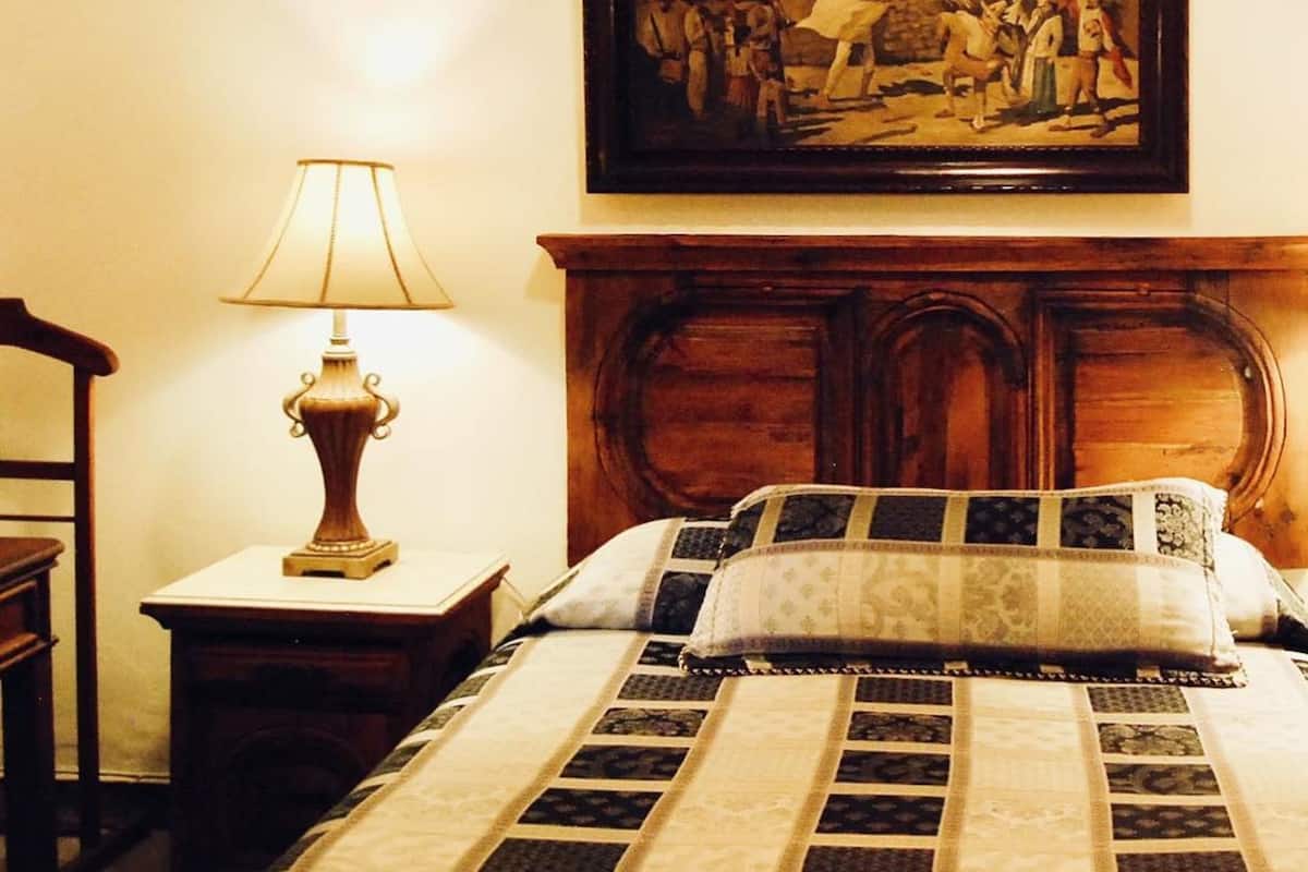 Una habitación de hotel con una cama, una mesita de noche con una lámpara y un cuadro en la pared.