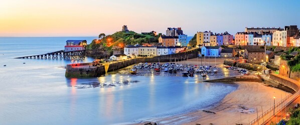 A coastal town with a historic fortification, colorful buildings, and a pier extending into calm waters.