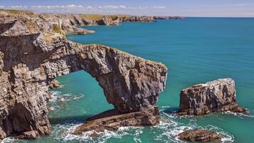 A coastal landscape with a prominent rock formation creating a natural arch over the sea.