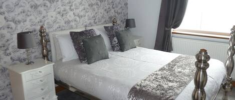 A neatly arranged bedroom with a large bed, two bedside tables, and a window with curtains.