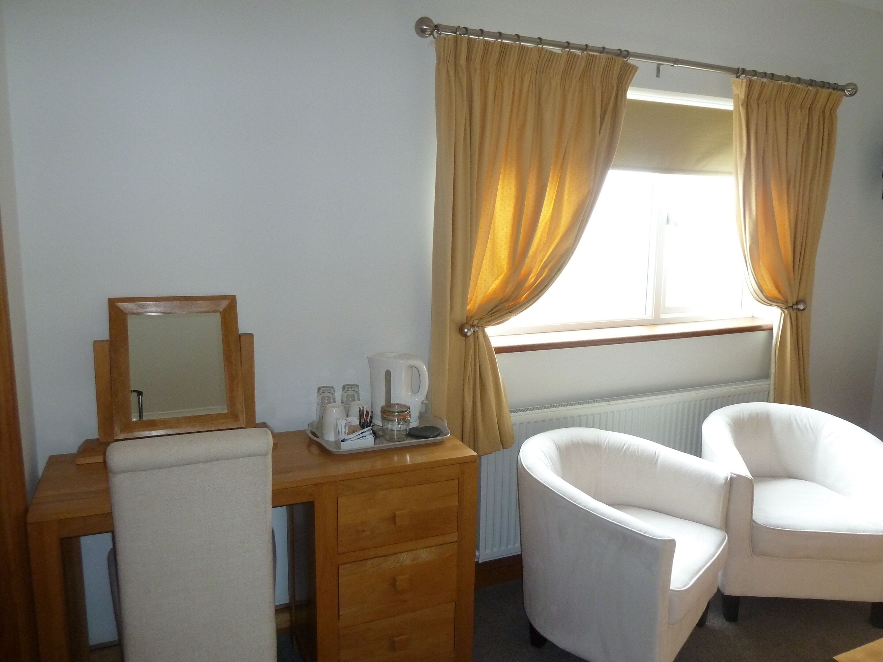 A hotel room with a wooden desk, a chair, a mirror, and a window with curtains.