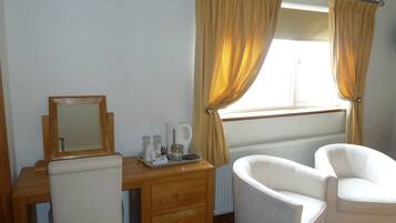 A hotel room with a wooden desk, a chair, a mirror, and a window with curtains.