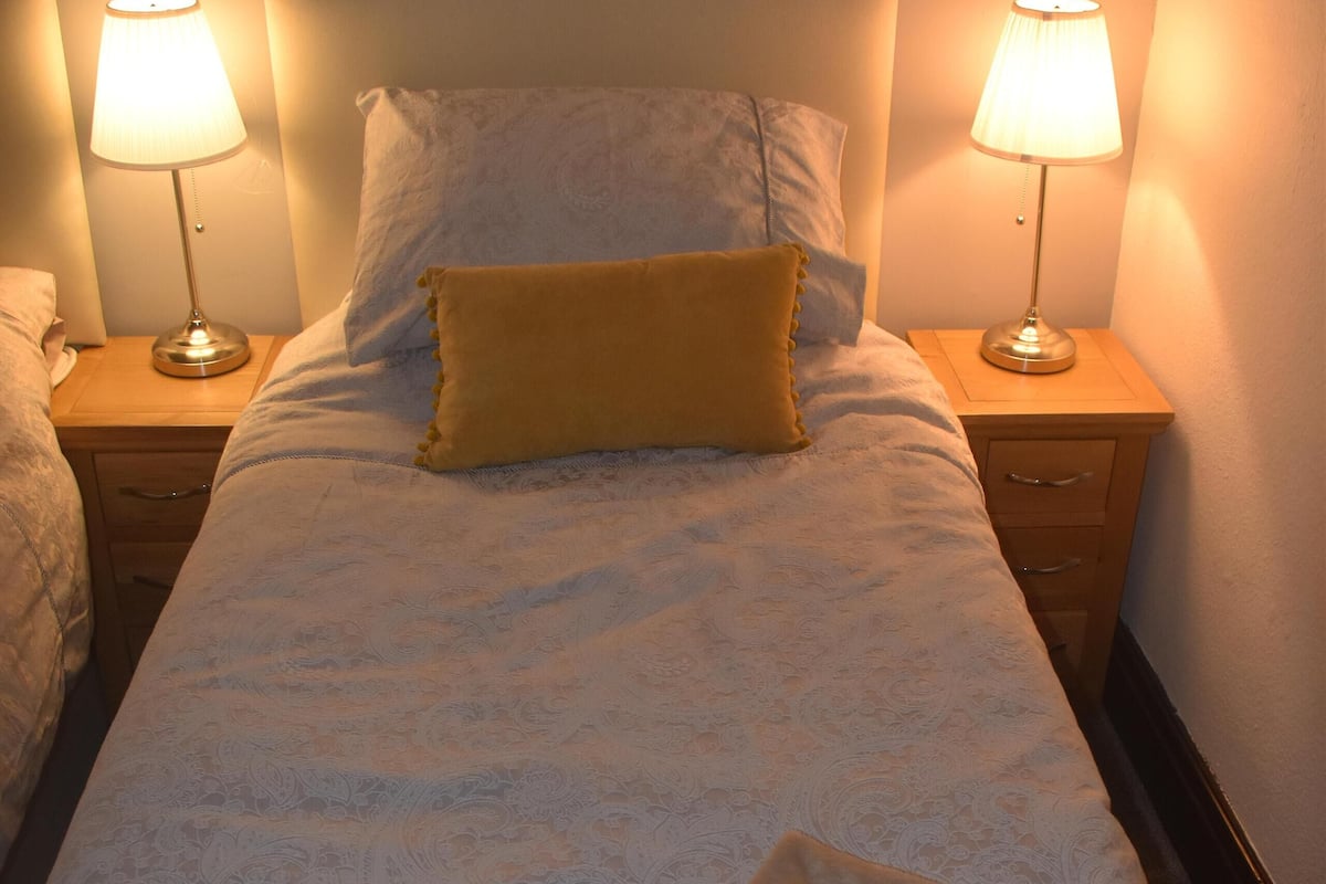 A neatly made bed with a patterned bedspread, two bedside lamps, and a wooden nightstand with drawers.