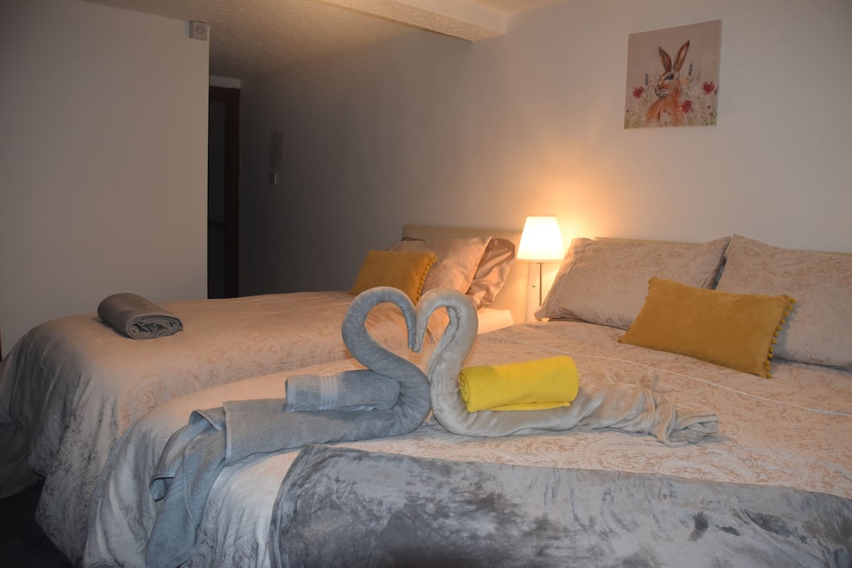 A hotel room with two beds, a painting on the wall, and a lamp on the nightstand.