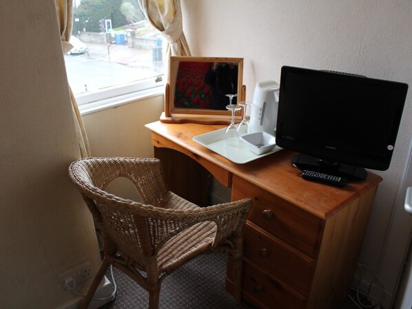 A small room with a wooden desk, a wicker chair, a framed picture, a computer monitor, and a tray with a glass and a cup. - The Avenue Restaurant at The Victoria Inn (Haddington)