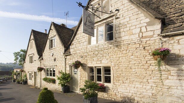 A stone building with a sign reading "The Bell" and flower baskets on the windowsills.