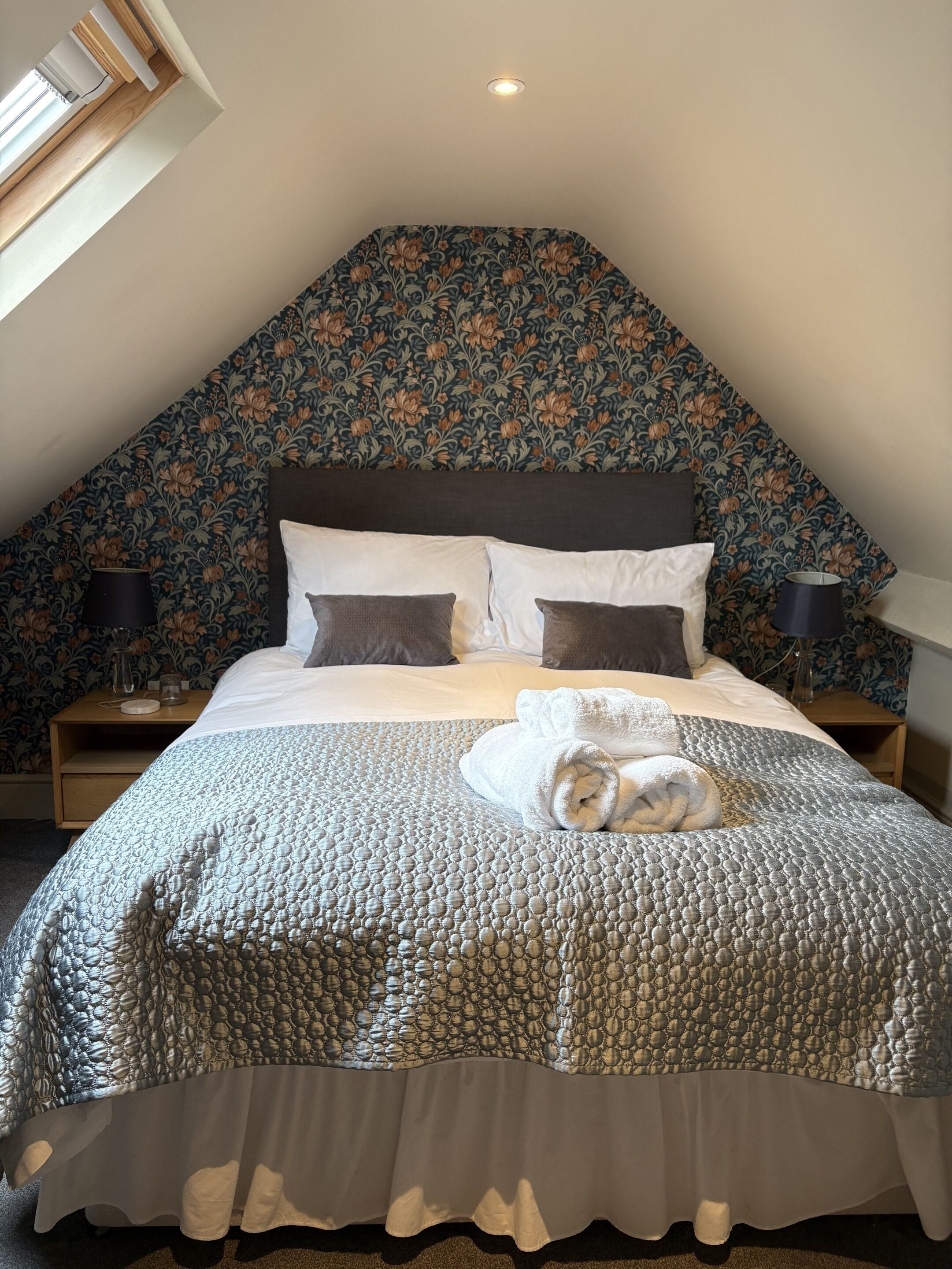 A bedroom with a large bed, floral wallpaper, and a skylight.