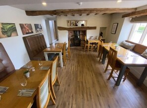 A cozy restaurant with wooden tables and chairs, a brick fireplace, and framed pictures on the walls.