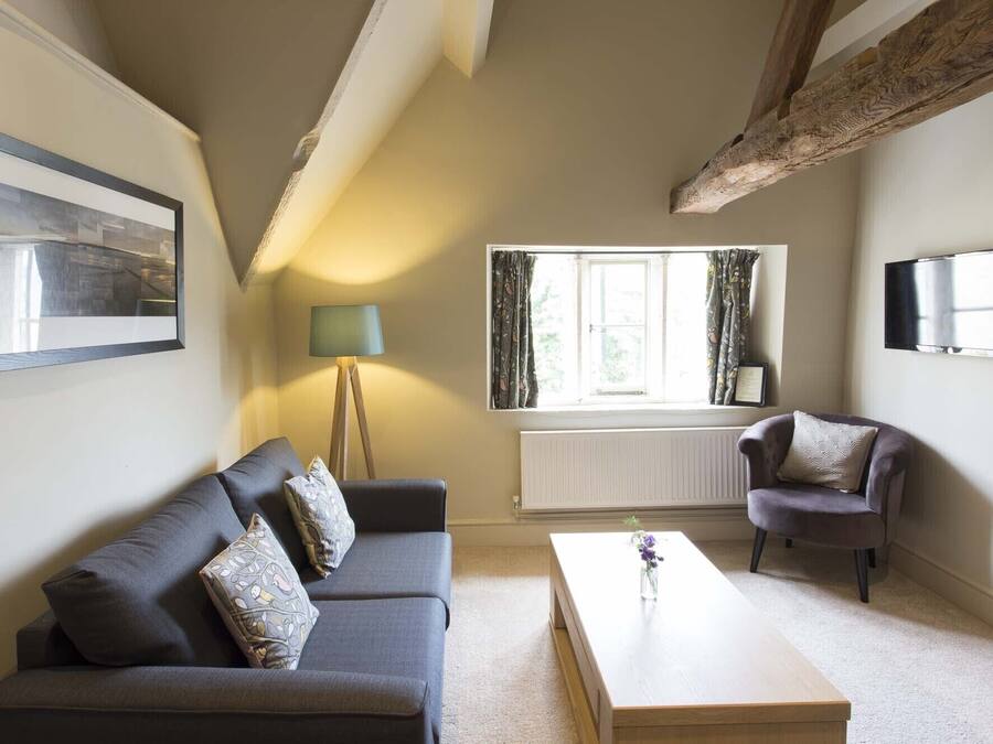A living room with a sofa, armchair, coffee table, lamp, window, radiator, and a painting on the wall.