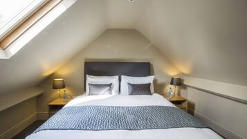 A bedroom with a sloped ceiling, a bed with white bedding, two bedside tables with lamps, and a skylight.