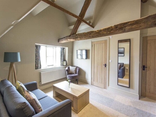 A cozy living room with a sofa, coffee table, and a lamp. There is a window with curtains, a door, and a mirror on the wall. - The Bell Inn (Stroud)