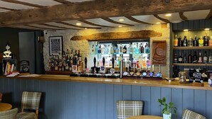 A bar area with wooden beams, a counter with various bottles, and plaid chairs.