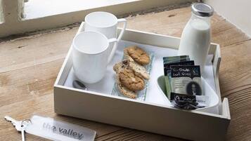 A tray with white mugs, cookies, a milk bottle, and a keychain labeled "the valley" on a wooden surface near a window.