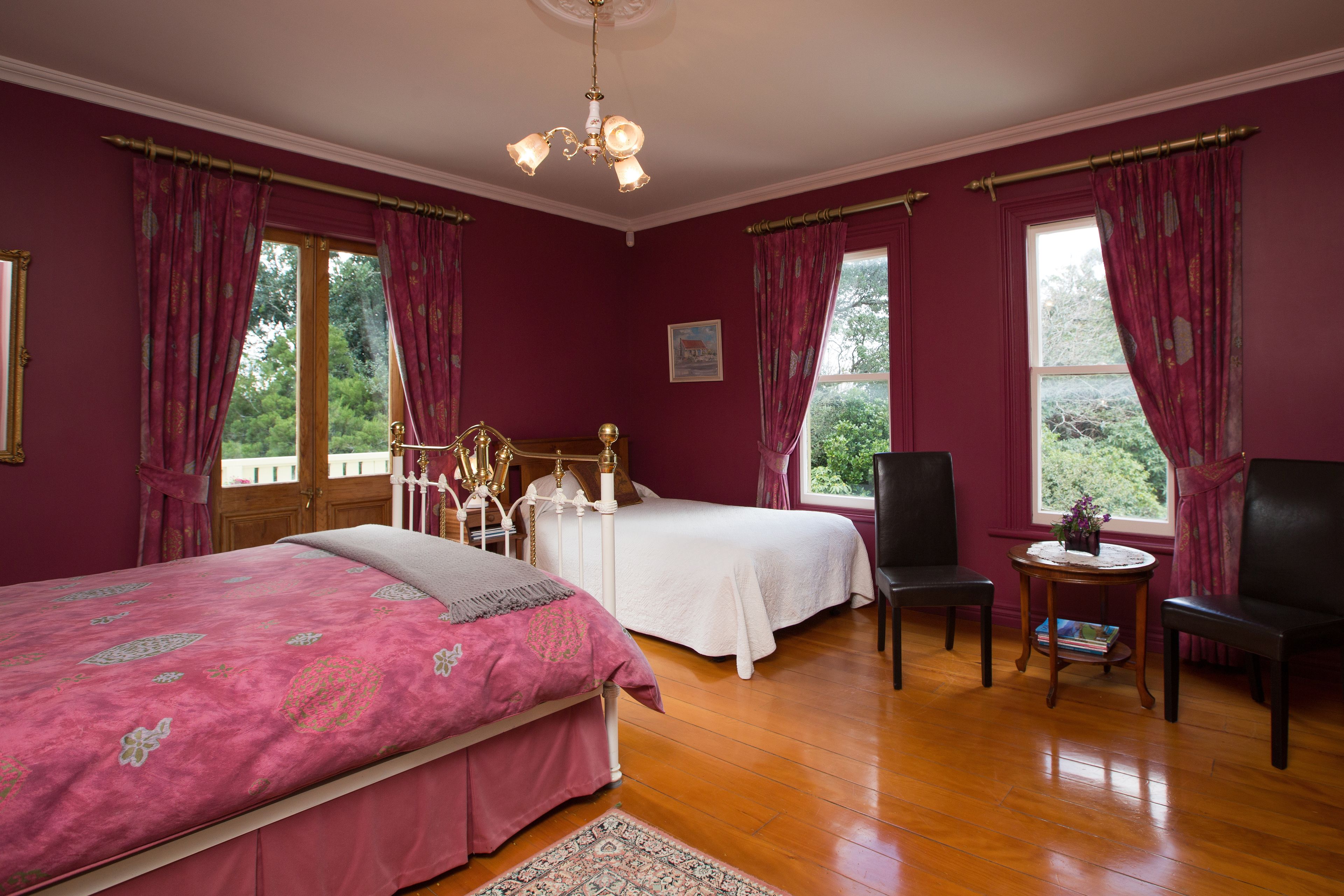 A room with two beds, a chandelier, and a view of greenery outside.