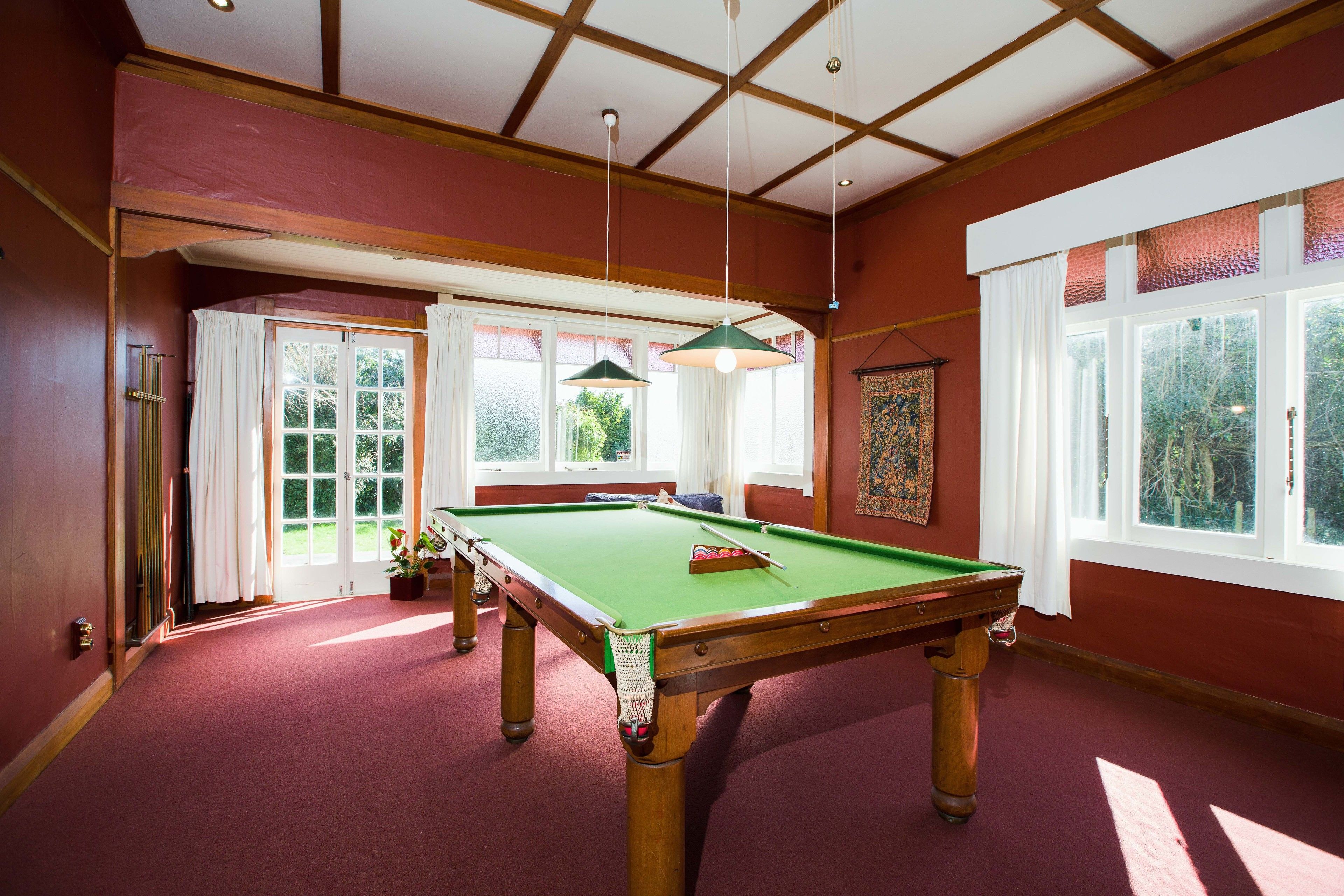 A pool table in a room with red walls, large windows, and a high ceiling.