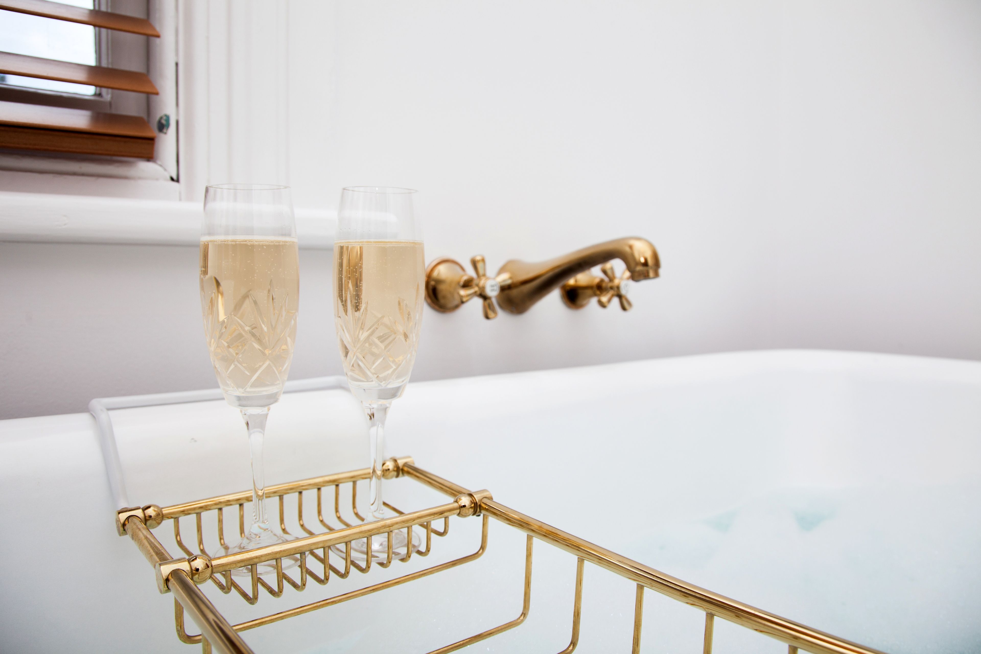 A gold-colored tray with two glasses of champagne on a white bathtub.