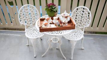Two ornate white chairs with a white table between them, holding a tray with tea cups, teapot, sugar bowl, and a flower vase.