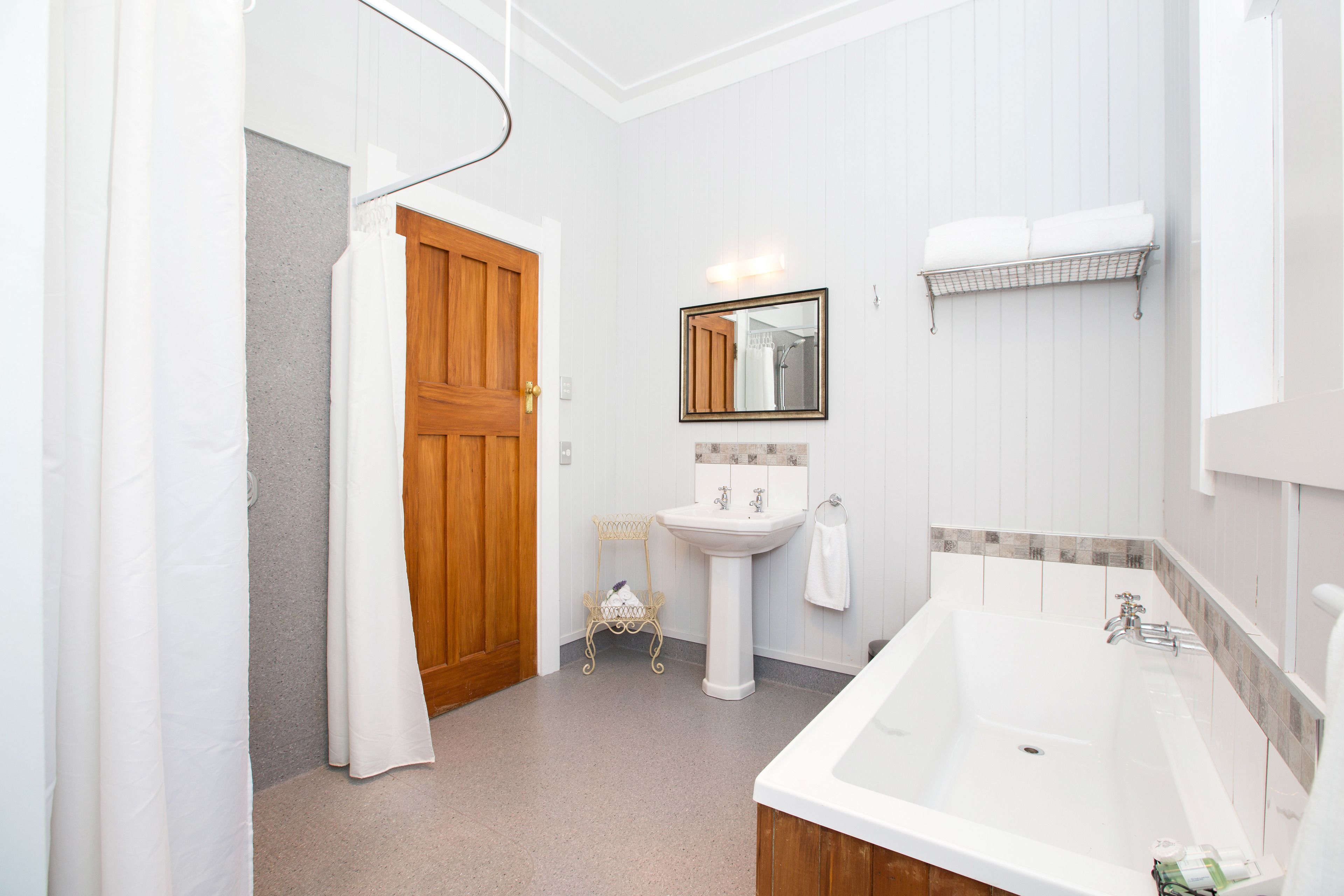 A bathroom with a wooden door, a white sink, a mirror, and a bathtub.