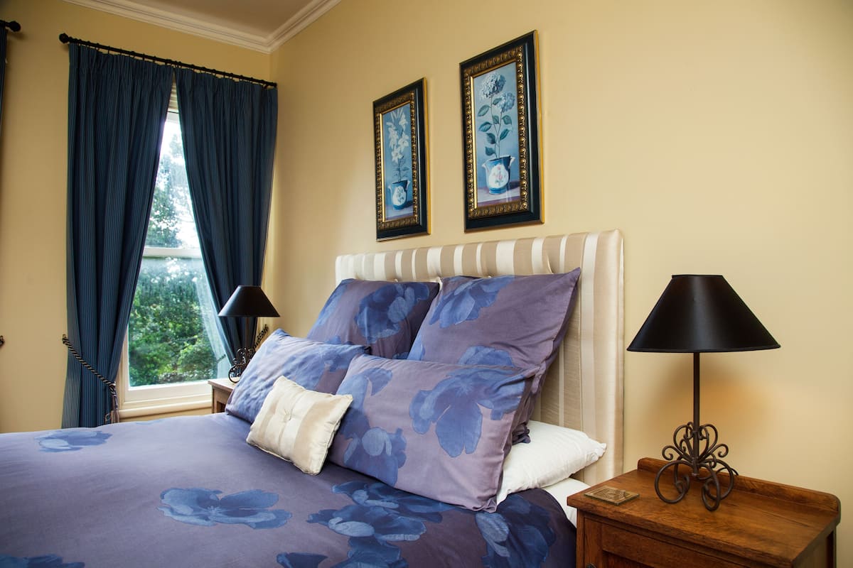 A bedroom with a bed, curtains, a nightstand, a lamp, and two framed pictures on the wall.