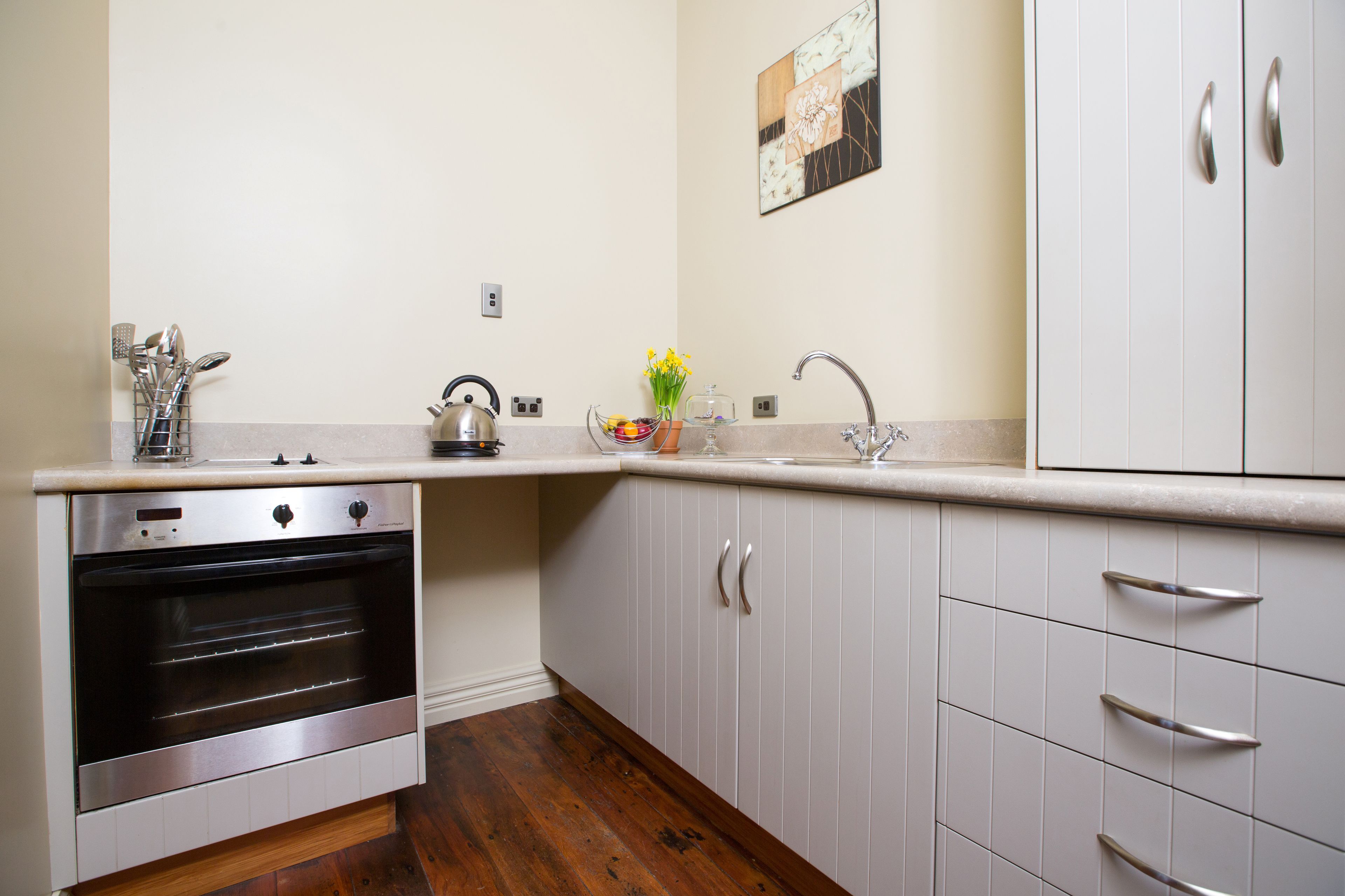 A kitchen with white cabinets, a stainless steel oven, a sink, and a kettle.