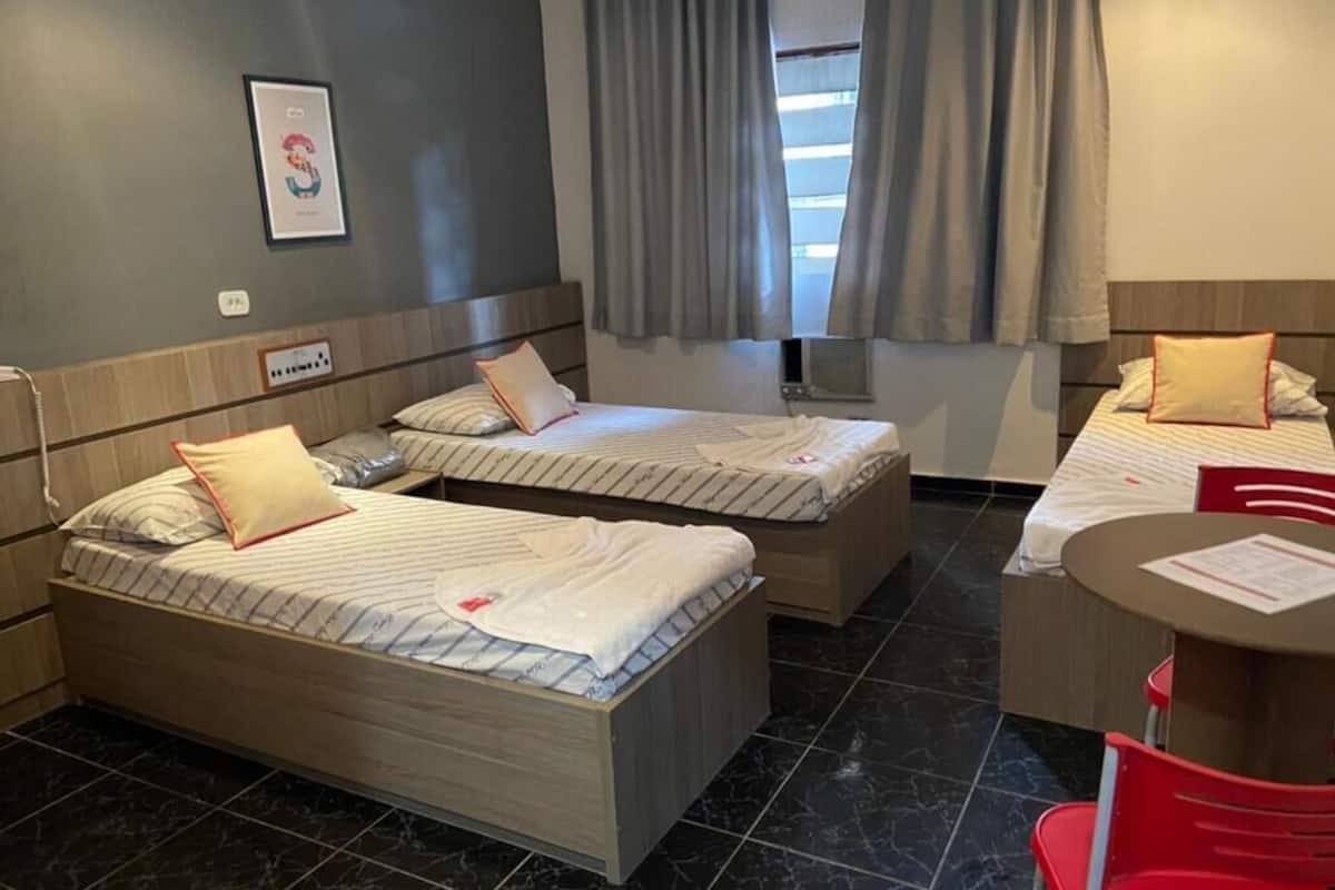 A hotel room with two single beds, a small table, and a chair.