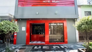 A hotel entrance with a red and grey facade, a glass door, and a contact number. - Hotel Belém (São Paulo)