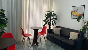A living room with a black sofa, red chairs, a round table, and a large potted plant. - Hotel Belém (São Paulo)