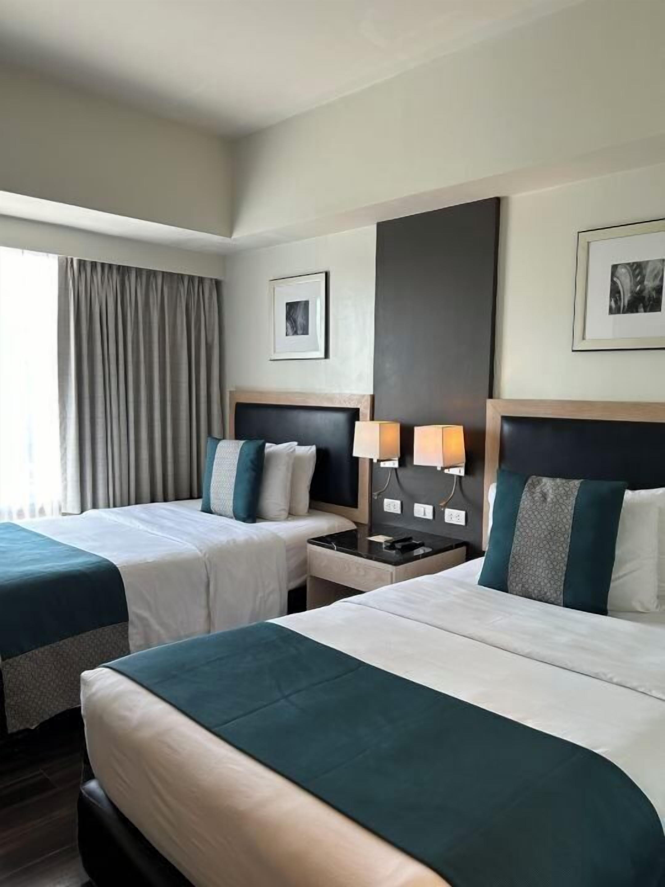 Habitación de hotel con dos camas, una mesita de noche, una lámpara y un cuadro en la pared.