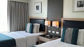 Habitación de hotel con dos camas, una mesita de noche, una lámpara y un cuadro en la pared.