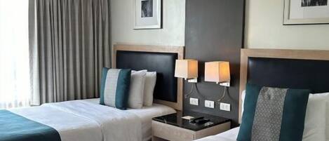 A hotel room with two beds, a nightstand, a lamp, and a framed picture on the wall.