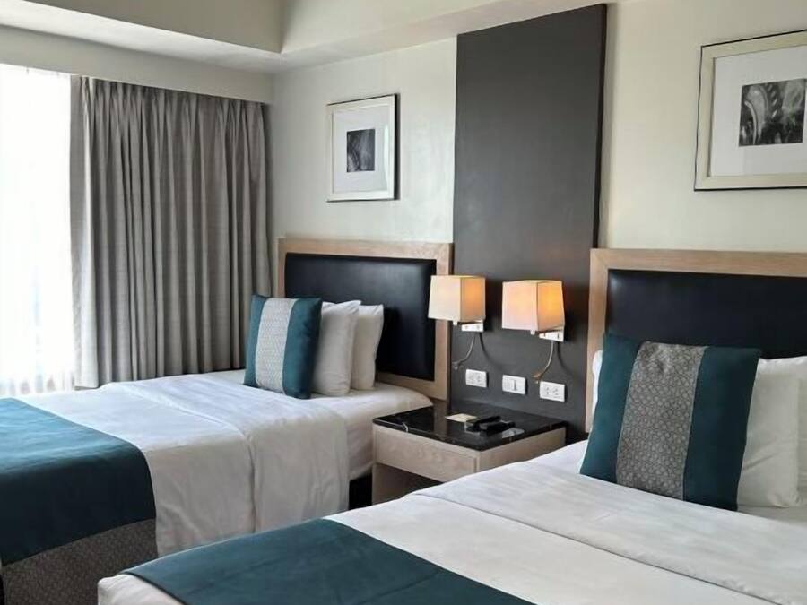 Habitación de hotel con dos camas, una mesita de noche, una lámpara y un cuadro en la pared.