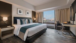 A modern hotel room with a large bed, a desk, and a view of the city.