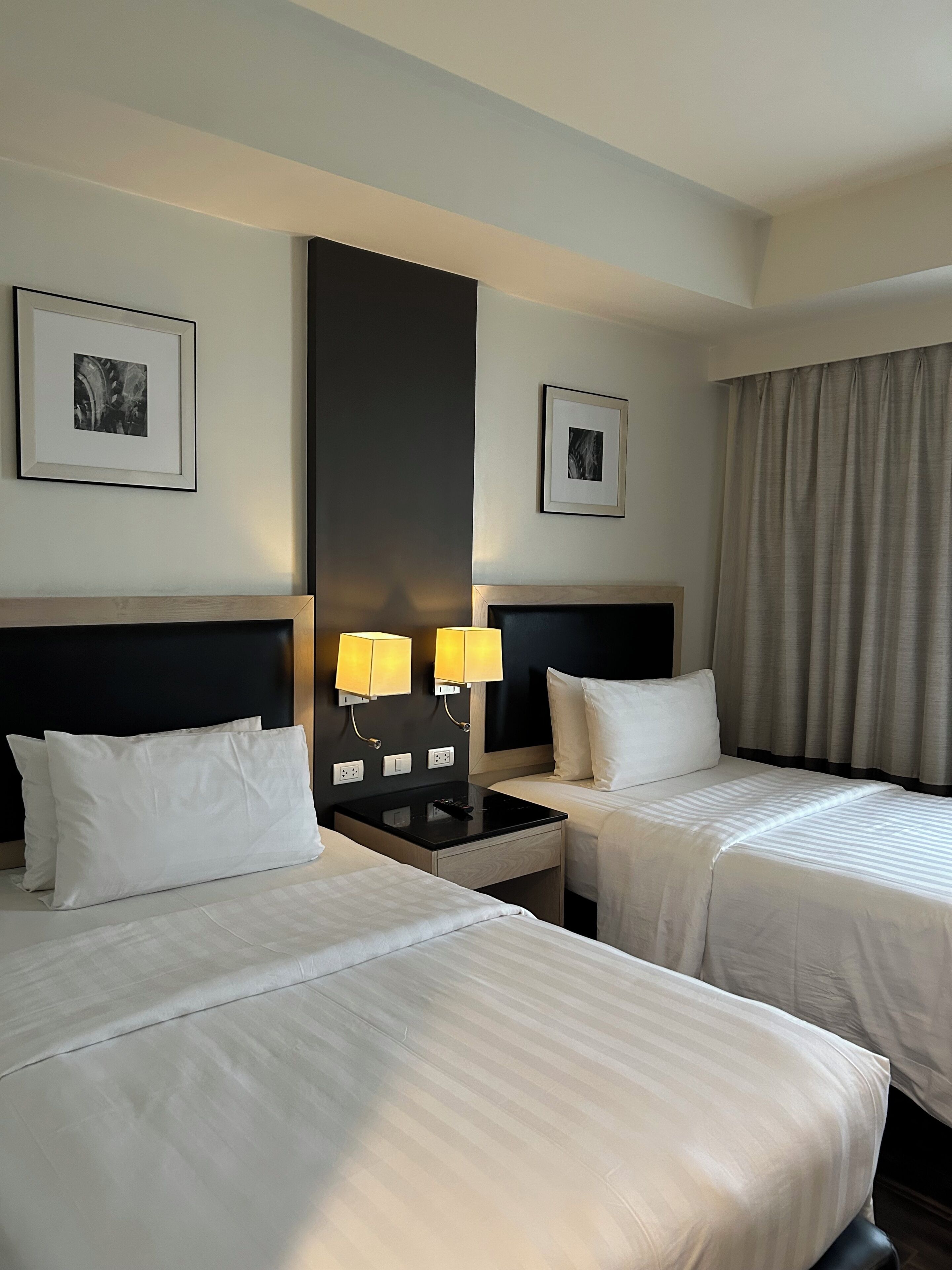 Una camera d'albergo con due letti, un comodino, due lampade a parete e due quadri appesi alle pareti.