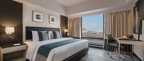 A modern hotel room with a large bed, a desk, and a view of the city.