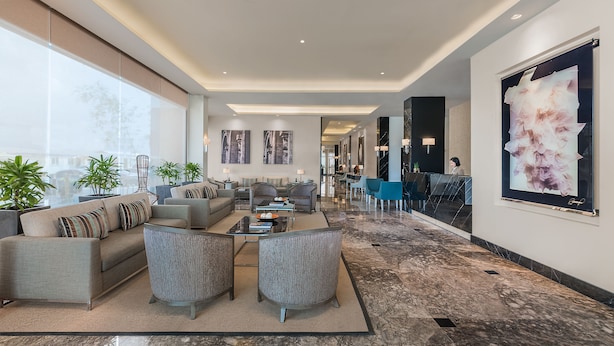 A spacious lobby with a modern design, featuring a seating area with sofas and armchairs, a reception desk, and a large abstract painting on the wall.