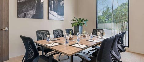 A conference room with a long table, six chairs, a potted plant, and two large windows.