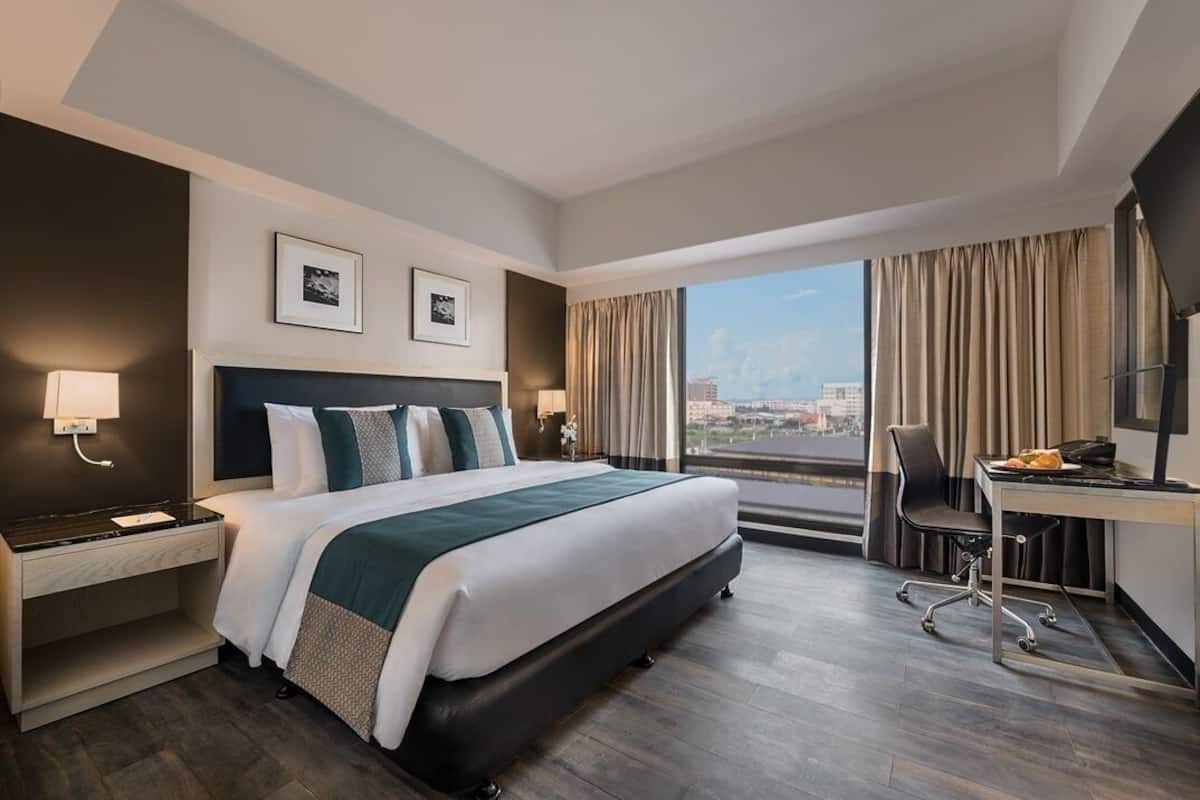 A hotel room with a large bed, a desk, a chair, and a view of the city.