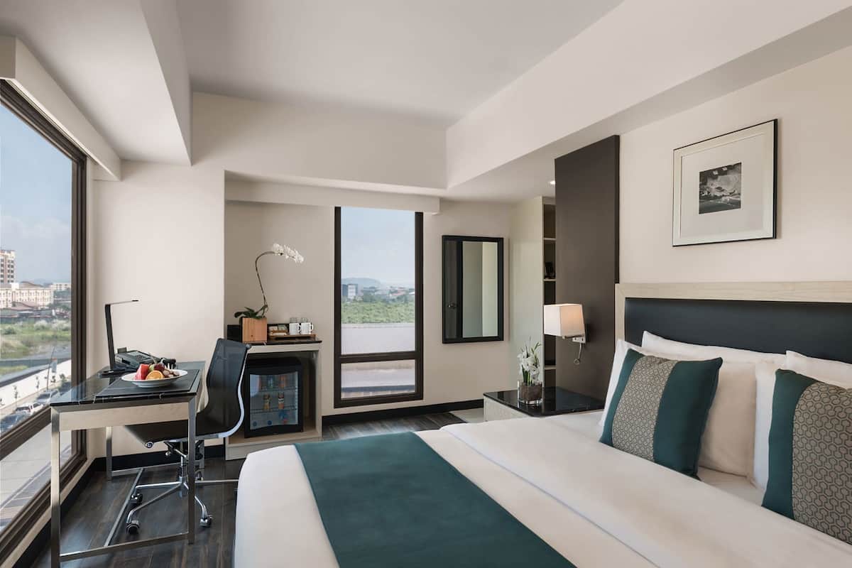 A hotel room with a bed, desk, and large windows offering a city view.