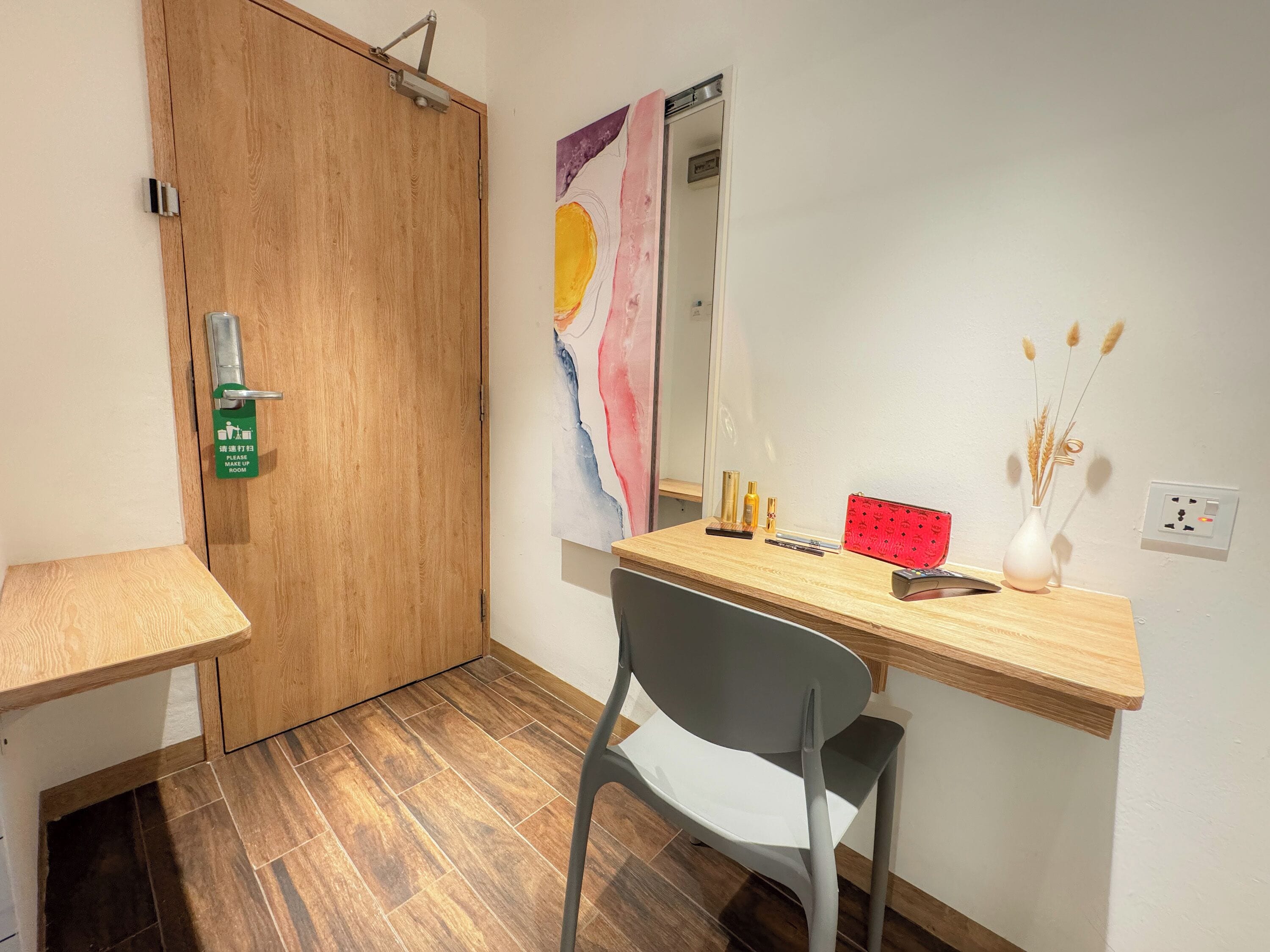 Ein Zimmer mit einem Holztisch, einem Stuhl, einem Spiegel und einer Tür mit einem grünen Schild.