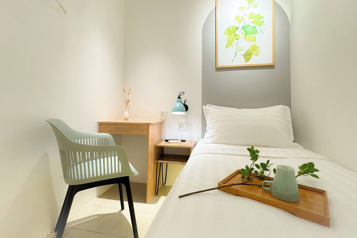 A neatly arranged hotel room with a bed, a desk, a chair, and a bedside table.